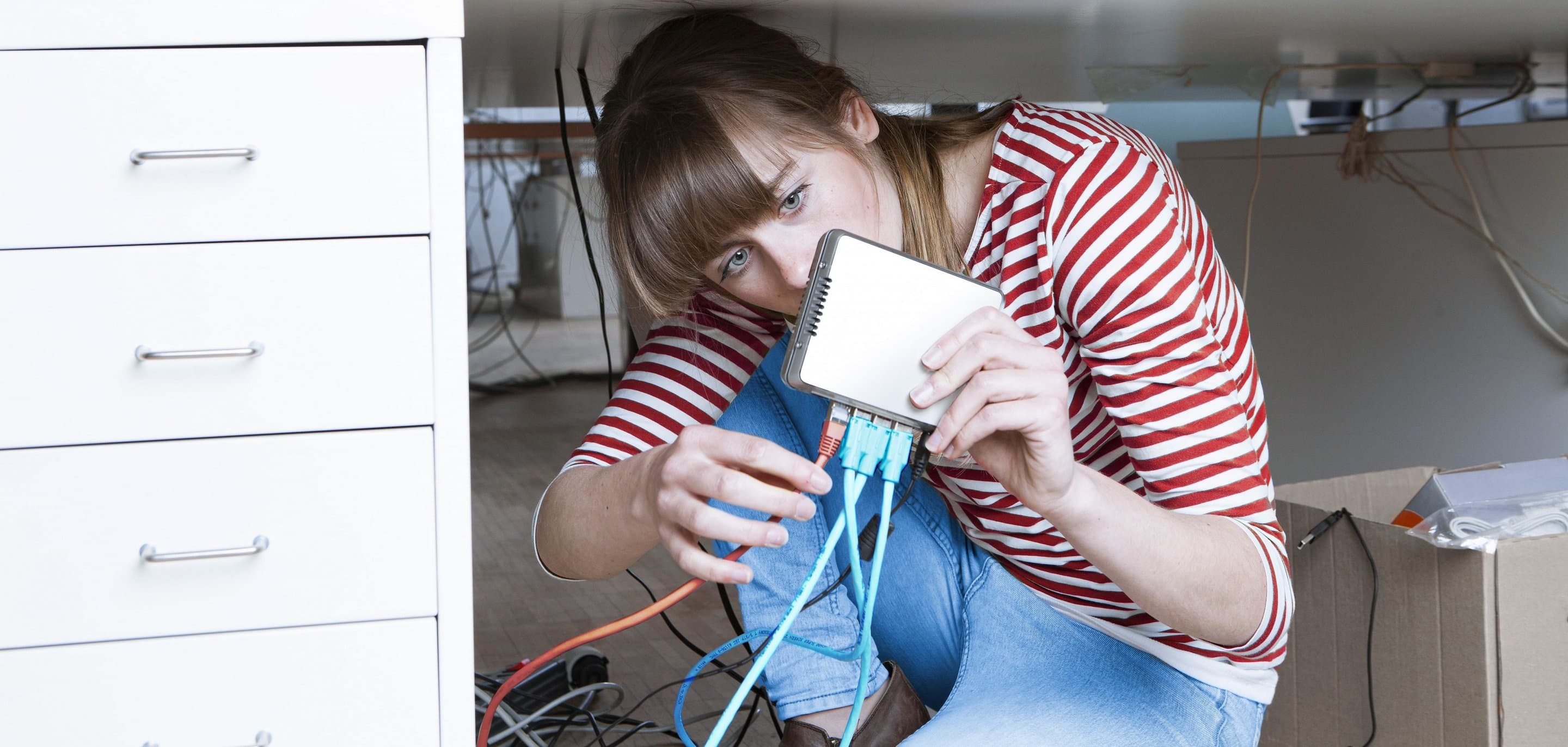 NetCologne Service und Hilfe Frau sitzt unter Schreibtisch und steckt ein Kabel in einen Router