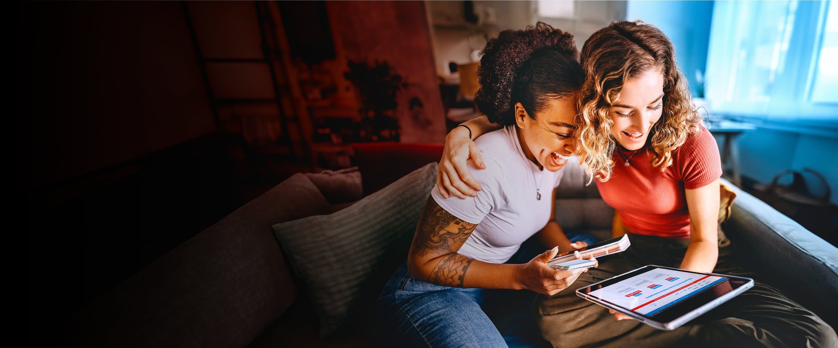 Zwei Frauen sitzen auf einem Sofa und schauen gemeinsam auf ein Tablet.