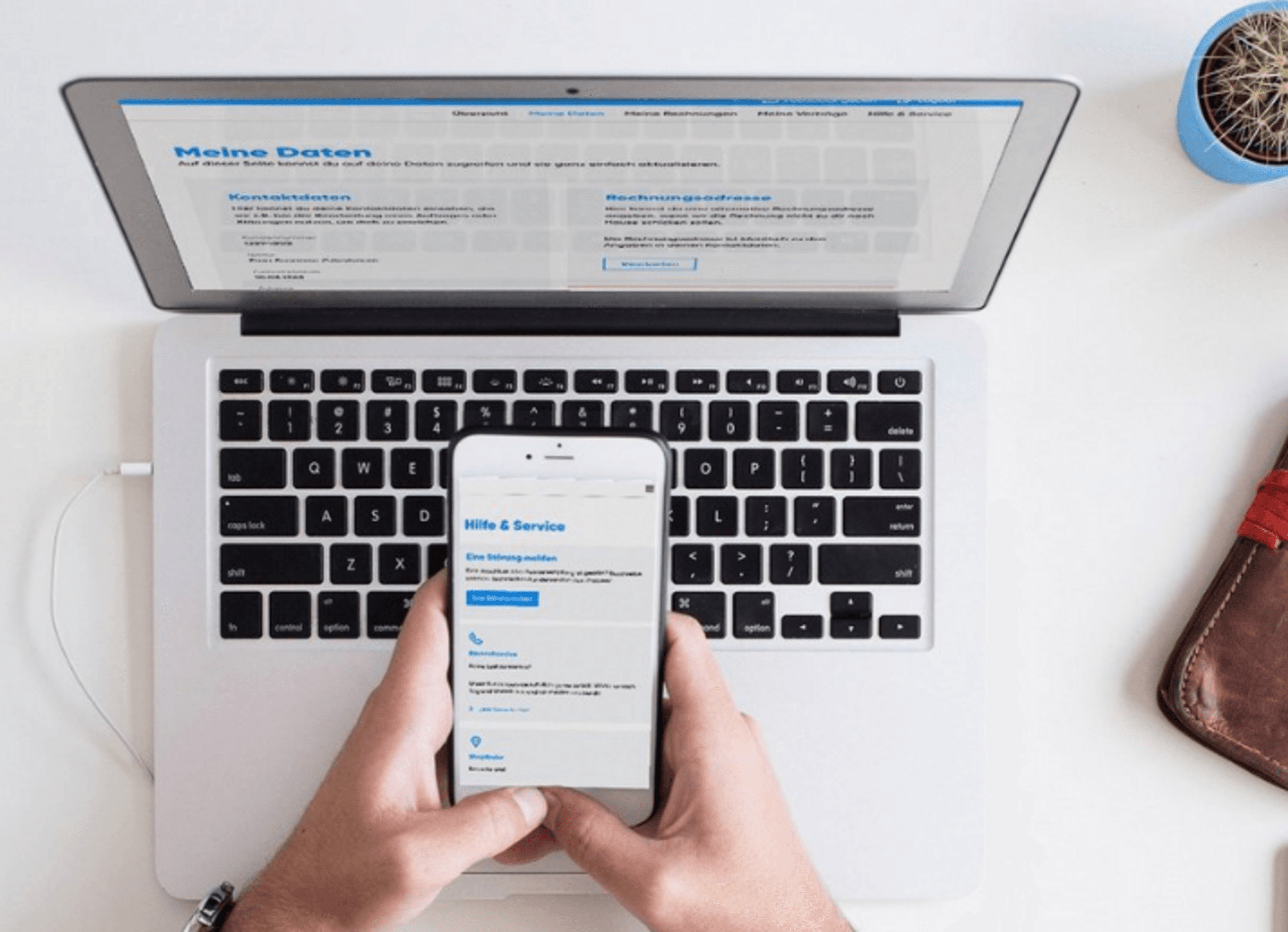 MeineKundenwelt LogIn Hände einer Person, die ein Smartphone vor einem Laptop halten und in MeineKundenwelt eingeloggt sind