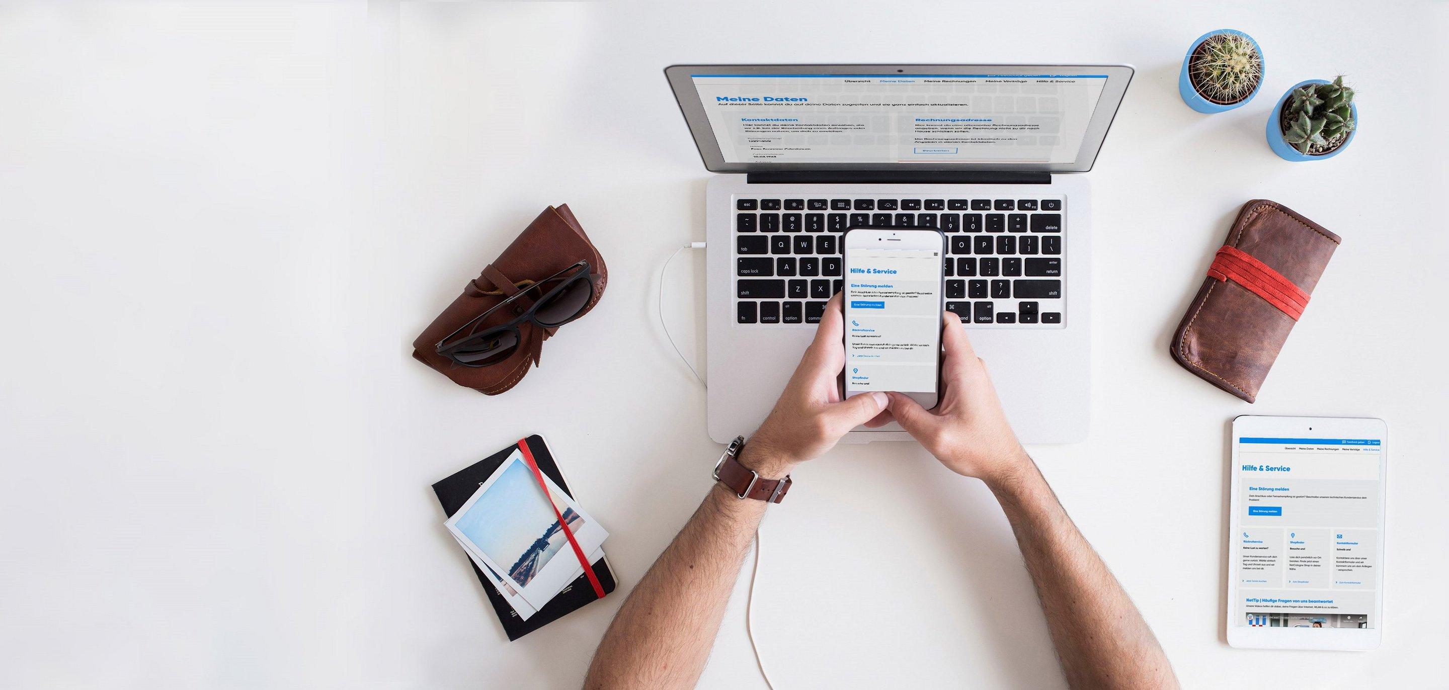 "MeineKundenwelt" Login Mann hält Handy vor Laptop und loggt sich in "MeineKundenwelt" ein