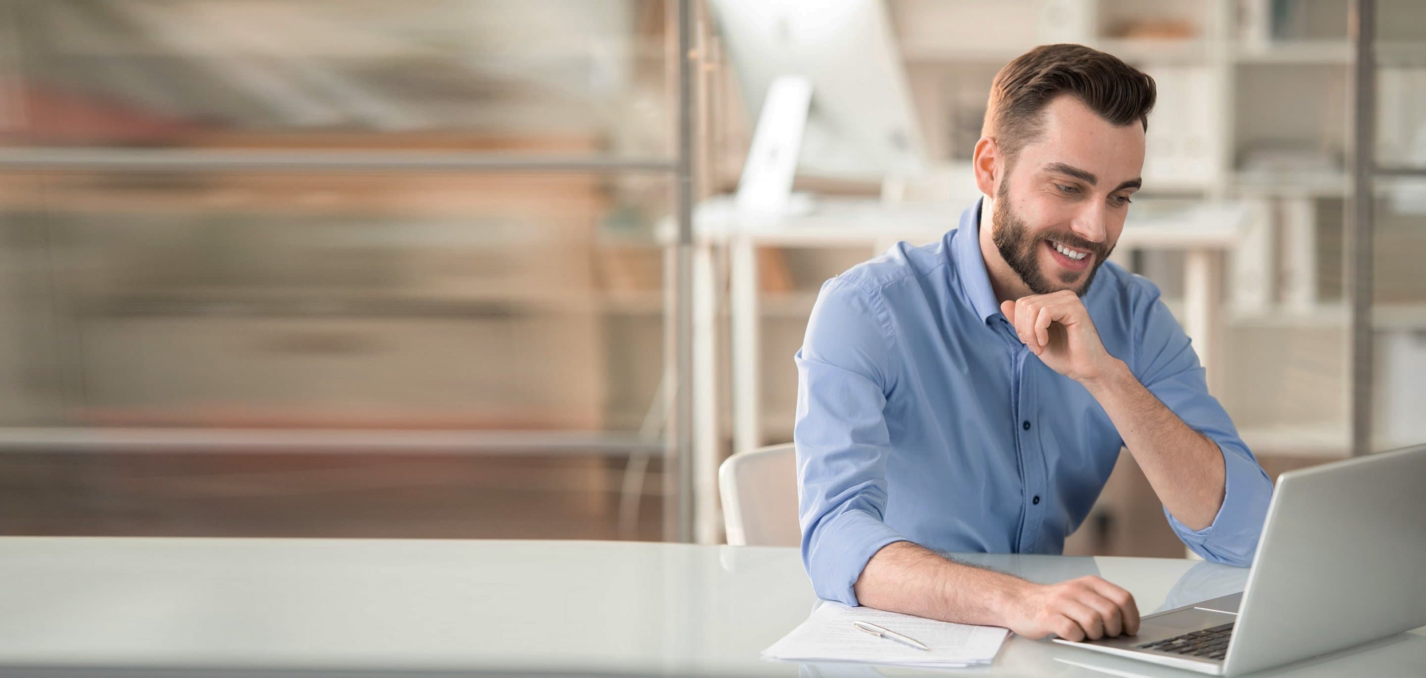 Digitale und analoge Tools im Einsatz Person sitzt am Schreibtisch mit Laptop, Unterlagen und Stift in einem Büro mit Regalen im Hintergrund.