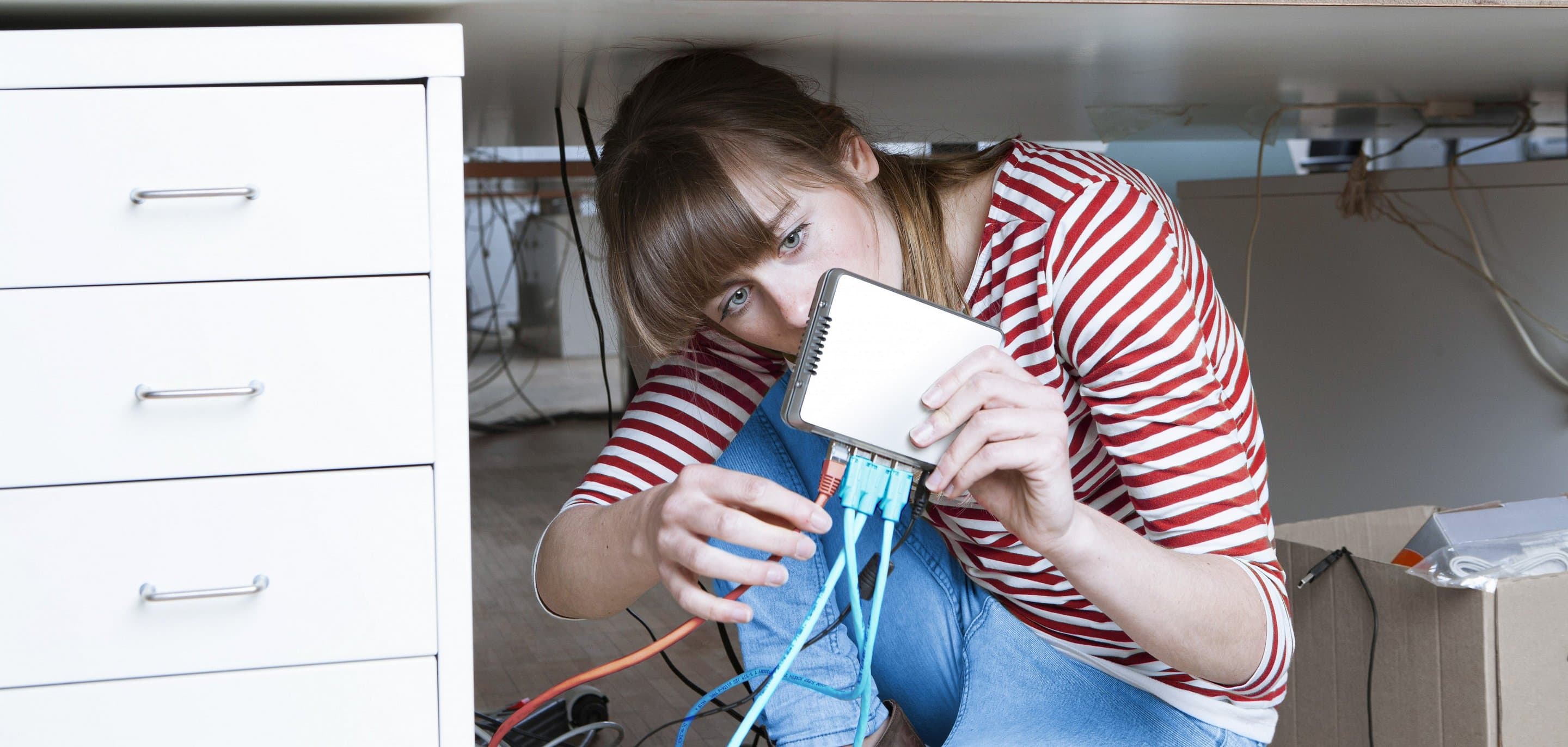 Service & Hilfe Frau sitzt unter einem Schreibtisch und steckt ein LAN-Kabel in einen Router