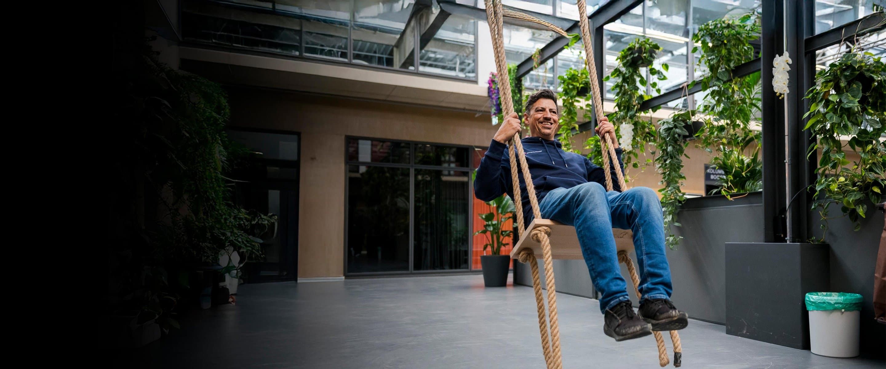 Symbolbild für Referenzkunde smartvillage Ein Mann auf einer Schaukel, die von der Decke eines großen Raumes hängt.