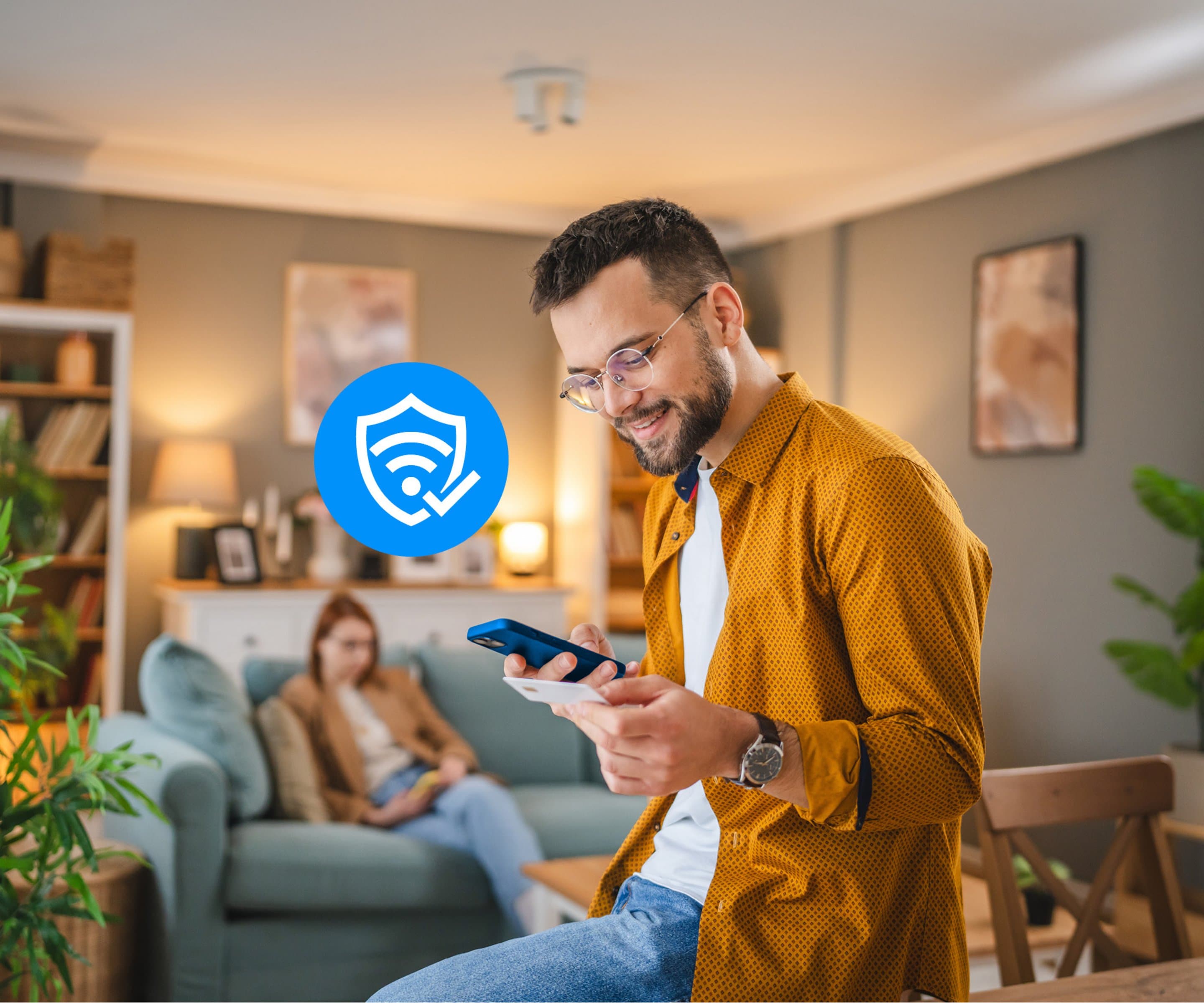 Sicherheit im Netz Mann im Vordergrund gibt Kreditkarteninformationen im Smartphone ein, im Hintergrund surft Frau auf dem Smartphone im Netz und sitzt auf der Couch.